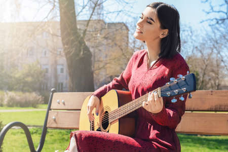 Beautiful young woman playing guitar on bench in park