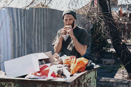 Poor homeless man near trash bin outdoorsの写真素材
