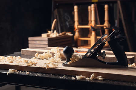 Carpenter's smoothing plane with wooden plank on table in workshop