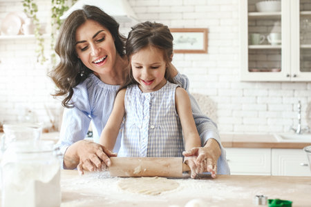 Happy mother with daughter preparing cookies in kitchen at homeの写真素材