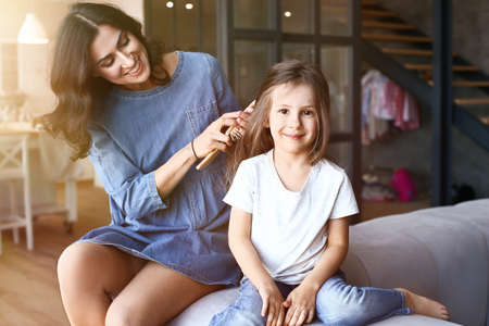 Mother brushing hair of her cute little daughter at homeの写真素材