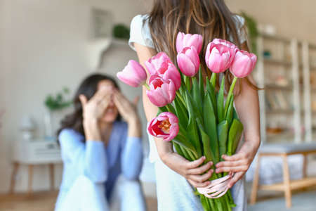 Little girl holding bouquet of flowers for mother behind her back at homeの写真素材