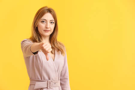 Portrait of mature woman showing thumb-down on color backgroundの写真素材