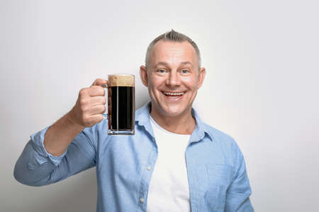 Happy middle-aged man with glass of beer on light background