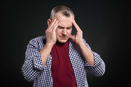 Handsome middle-aged man suffering from head ache on dark background