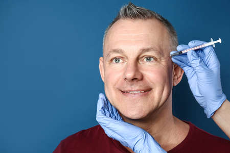 Middle-aged man and hands holding syringe for anti-aging injections on color backgroundの写真素材