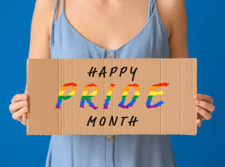 Young woman holding paper with text HAPPY PRIDE MONTH on color background