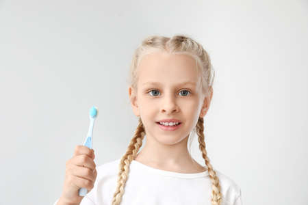 Little girl with toothbrush on light background