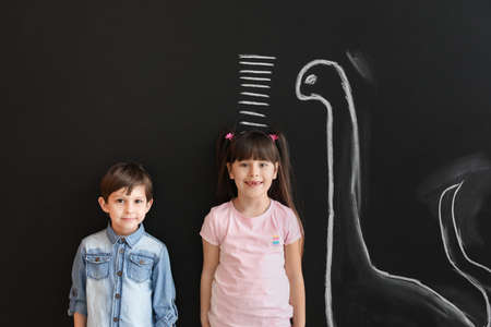 Cute little children measuring height near wall with marks and drawn dinosaurの写真素材