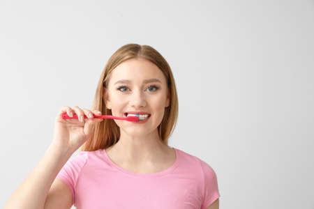 Beautiful woman cleaning teeth on light background