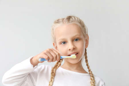 Little girl cleaning teeth on light background