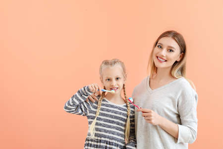 Little girl and her mother cleaning teeth on color backgroundの写真素材