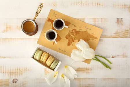 World map with tulip flowers, macarons and coffee on white wooden table