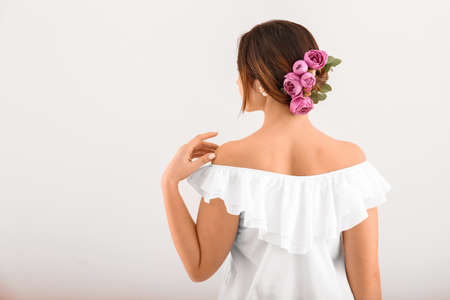 Young woman with beautiful flowers in her hair on light background, back view