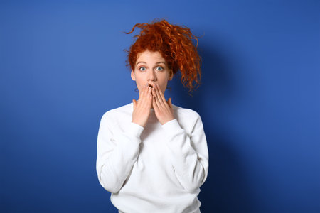 Shocked redhead woman on color background