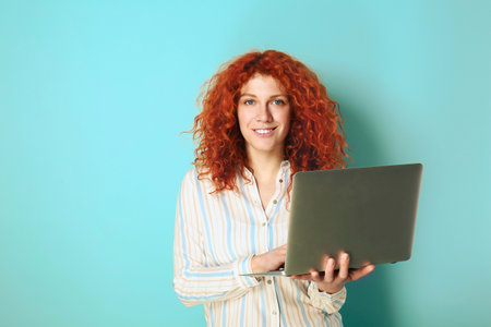 Beautiful redhead woman with laptop on color backgroundの写真素材