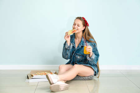 Beautiful woman eating tasty near light wall
