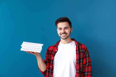 Handsome young man with books on color backgroundの写真素材
