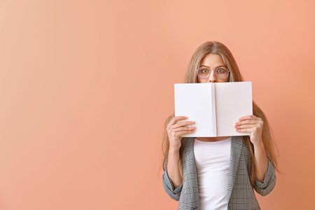 Shocked young woman with book on color background