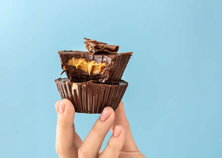 Female hand with chocolate butter cups on color background