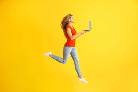 Beautiful jumping woman with laptop on color background