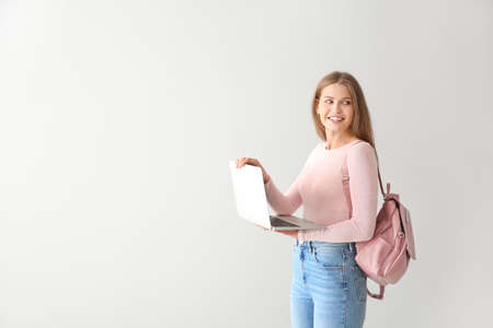 Female student with laptop on light background