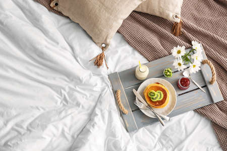 Tray with tasty breakfast and flowers on bed