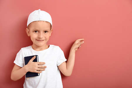 Little Muslim boy with Koran pointing at something on color background