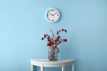 Vase with beautiful blossoming branches on table near color wall