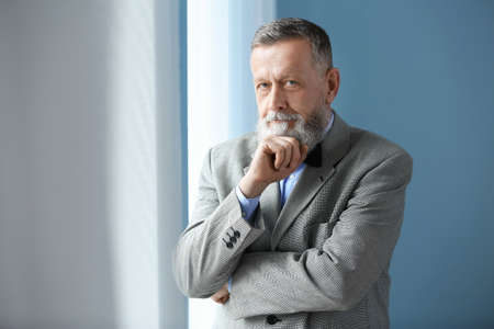 Portrait of handsome senior man near window at home