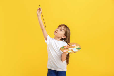Little girl with palette and brush on color background