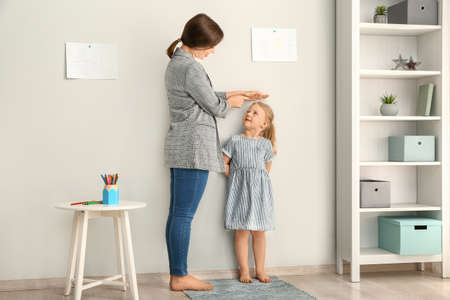 Mother measuring height of little girl near wallの写真素材