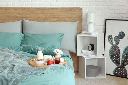 Tray with tasty breakfast on bed in interior of room