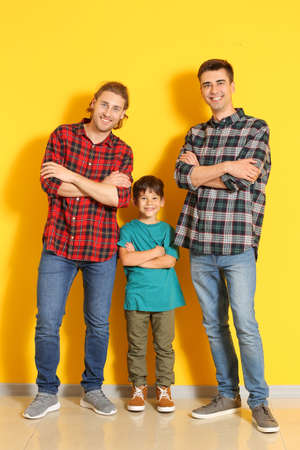 Happy gay couple with adopted child near color wall