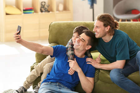Happy gay couple taking selfie with adopted child at home