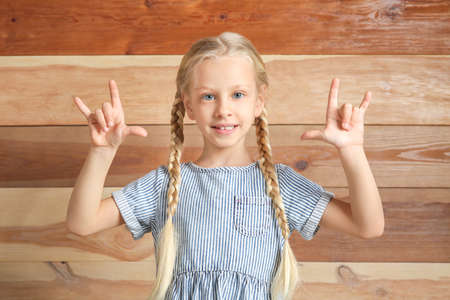 Little deaf mute girl using sign language on wooden backgroundの写真素材
