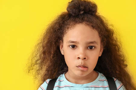 Funny African-American schoolgirl on color background