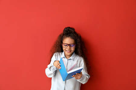 African-American girl with book on color background