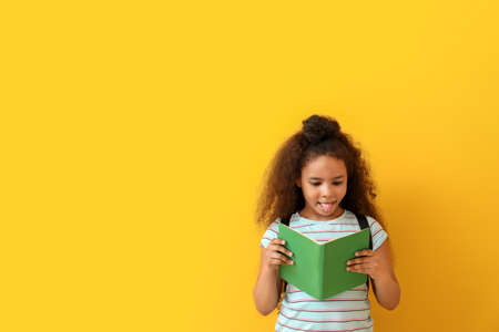 African-American girl reading book on color background
