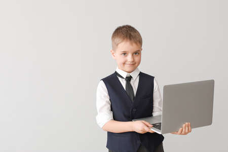 Cute little businessman with laptop on light background