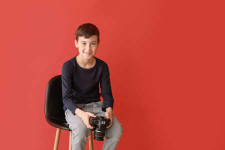 Cute little photographer sitting on chair against color background