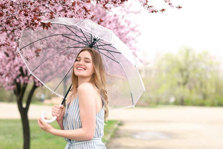 Portrait of beautiful young woman with umbrella in park on spring dayの写真素材