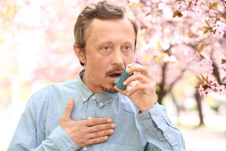 Man with inhaler having asthma attack on spring dayの写真素材