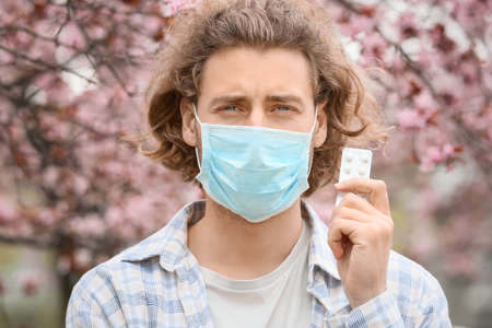 Young man in protective mask and with pills near blooming treeの写真素材