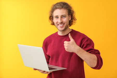 Male programmer with laptop showing thumb-up gesture on color backgroundの写真素材