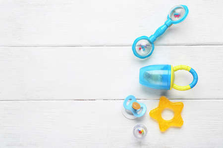 Baby nibbler, pacifier and rattle on white wooden tableの写真素材