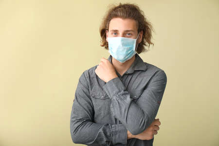 Young man wearing protective mask on color background