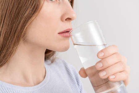 Woman drinking fresh water on light background, closeup