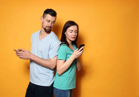Young couple with mobile phones on color background