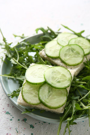 Plate with tasty cucumber sandwiches on light tableの写真素材